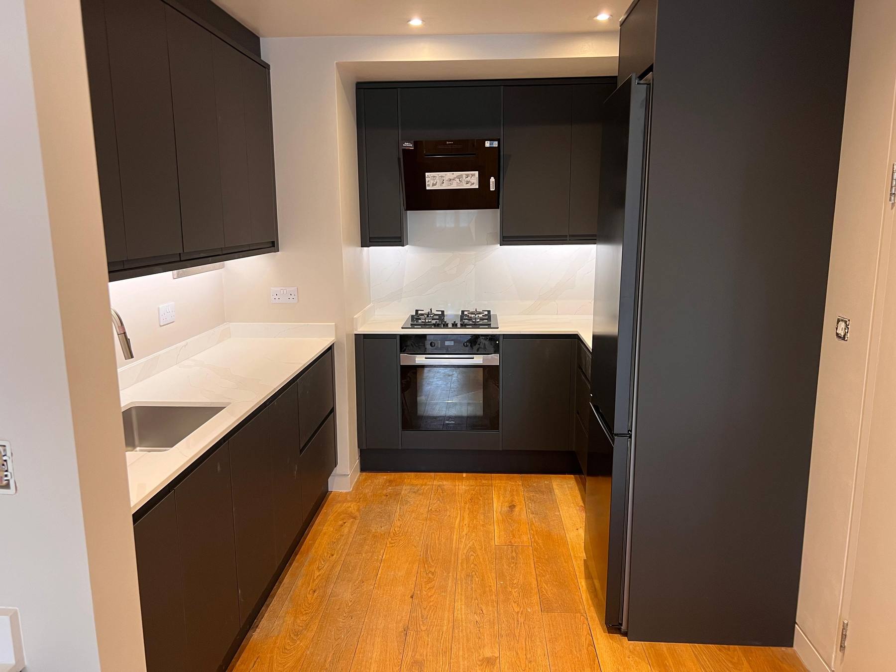 Dark handleless kitchen with oak flooring, by CVS Home Improvements